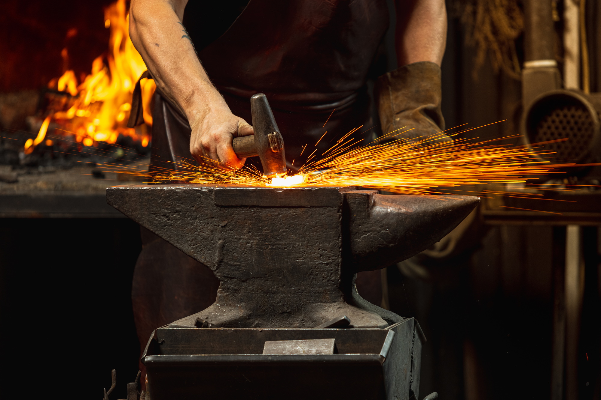 Close-up working powerful hands of male blacksmith forge an iron product in a blacksmith. Hammer